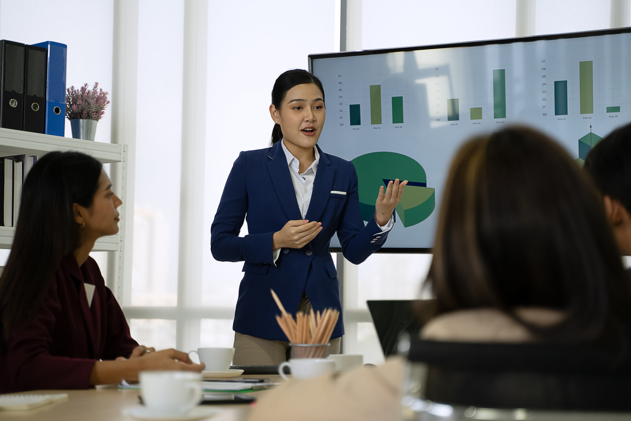 A young business professional taking charge of a corporate presentation, presenting pie charts and bar graphs on a big screen.