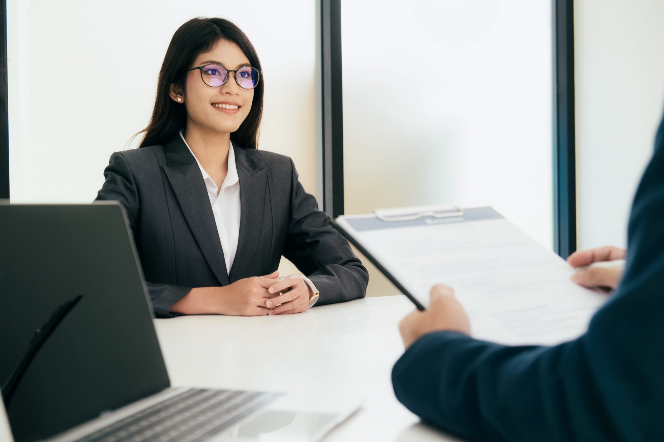 A young woman sitting across the table from her interviewer in a bright office setting.